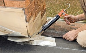 Roofer Applying Caulk to House Chimney Flashing