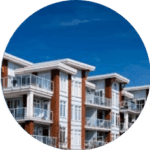 Modern apartment building with multiple floors featuring glass balconies and a combination of brick and white paneling. The structure, equipped with top-notch commercial roofing services, is set against a clear blue sky.