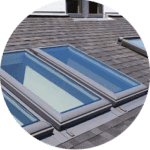Rectangular skylights grace the gray shingled roof provided by expert residential roofing services, offering a clear view of the blue sky through the glass.