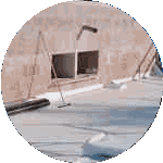 A rooftop scene features construction materials scattered about, alongside a paint roller on a pole and an unfinished wall with a rectangular opening. This light-colored setting, indicative of ongoing commercial roofing services, is filled with various tools and supplies.