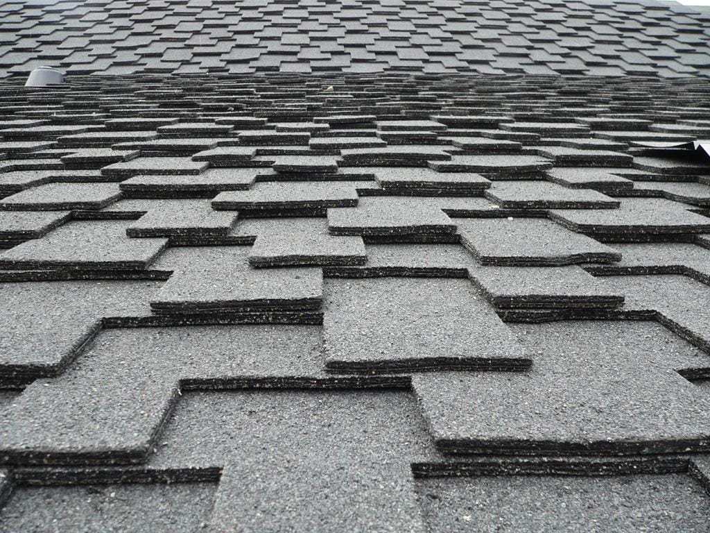 A close-up view of a roof today, covered with overlapping, textured gray shingles. Arranged in a staggered pattern, they create a layered, geometric effect, echoing the detail and uniformity often admired in cedar shake roofs.