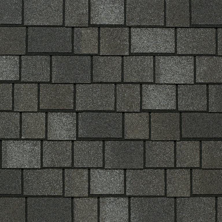 Close-up of a roof showcasing dark gray asphalt shingles arranged in a staggered pattern. The slightly rough texture and weathered appearance highlight variations that add depth and reflect superior shingle quality.