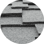 Close-up of stacked gray asphalt shingles, perfect for residential roofing services, showing their textured, granular surface. The shingles are arranged in an overlapping pattern, highlighting their layers and thickness.