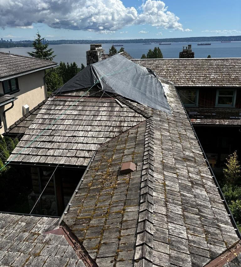 View of a wooden shake roof with a tarp, possibly awaiting a New Roof installation with CertainTeed Landmark Shingles, overlooking water and trees in West Vancouver under a partly cloudy sky. Date/time stamp: 2025-05-29, 3:21 PM.