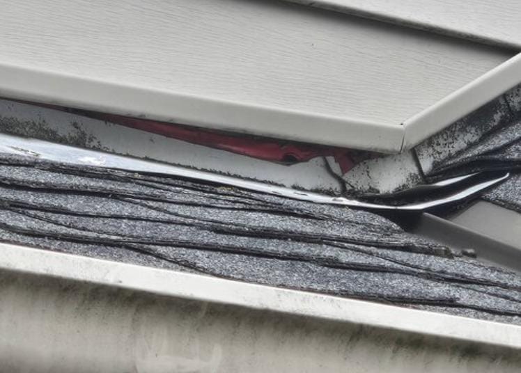 Close-up of a house roof showing damaged shingles and exposed underlayment, indicating the need for a roof replacement. Visible red sheathing and misaligned roofing materials near the gutter suggest it’s time to call Absolute Roof Solutions.